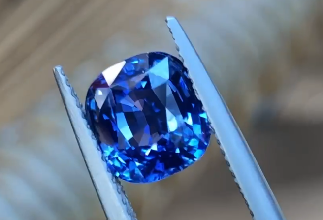 Emerald cut blue sapphire held in tweezers