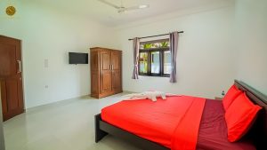 Villa Noble Horizon Sri Lanka interior – double guestroom with red bedding, wooden wardrobe, wall-mounted TV and garden view window